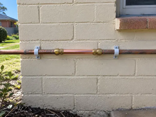 Repaired copper water pipe on a painted brick exterior wall in Bolwarra Heights