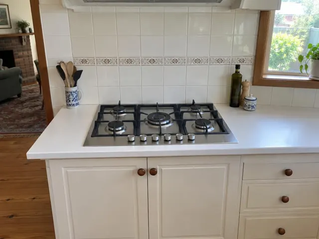 Stainless steel gas cooktop set into a white kitchen bench with tiled splashback in Mindaribba