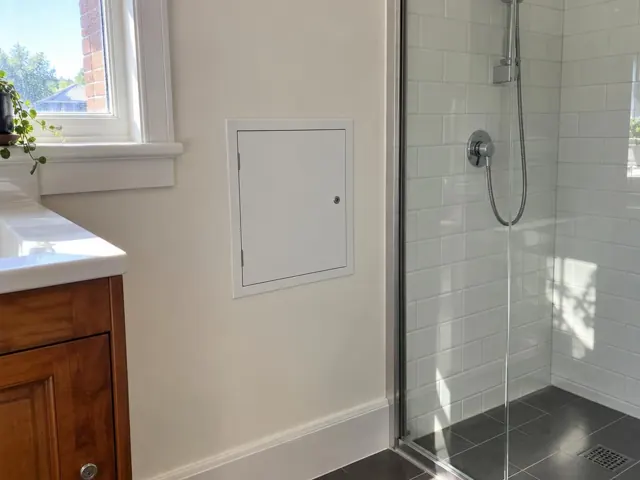 Small white access panel on a painted bathroom wall beside a tiled shower in Oakhampton