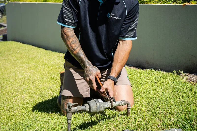 Plumber kneeling at a water meter on a front lawn